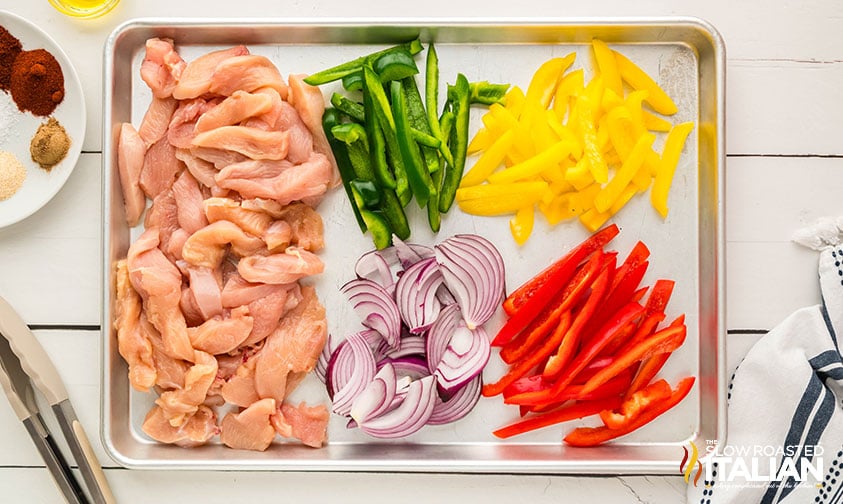 adding sliced chicken, bell peppers and onion to sheet pan for fajitas