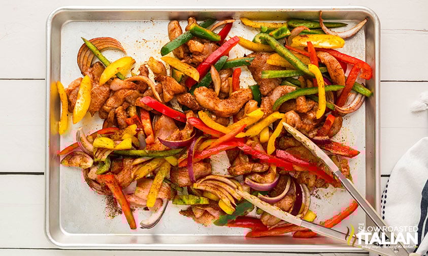tossing sheet pan chicken fajitas ingredients in olive oil and seasoning