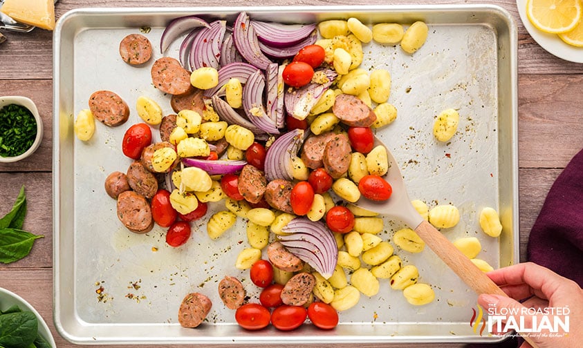 tossing sheet pan gnocchi ingredients in oil and seasonings