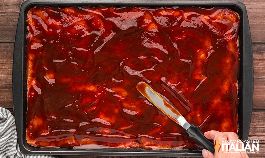 glaze added to meatloaf mixture on a sheet pan