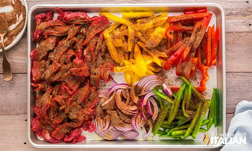 adding seasoning to steak fajitas ingredients on a sheet pan