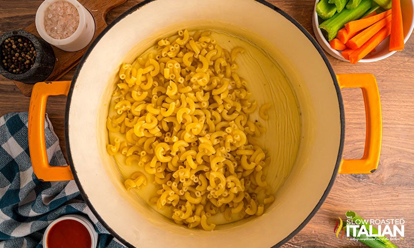 cooked macaroni noodles added to cheese sauce in pot