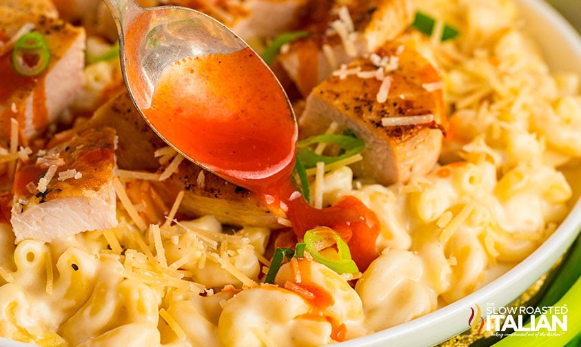 spooning buffalo sauce over chicken mac and cheese