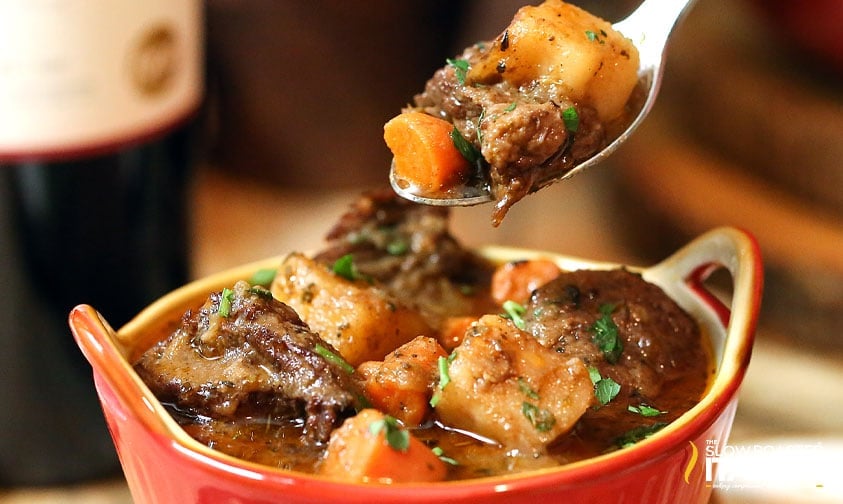 lifting a spoonful of hearty beef soup out of bowl
