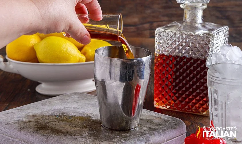 pouring amaretto into cocktail shaker from tall shot glass