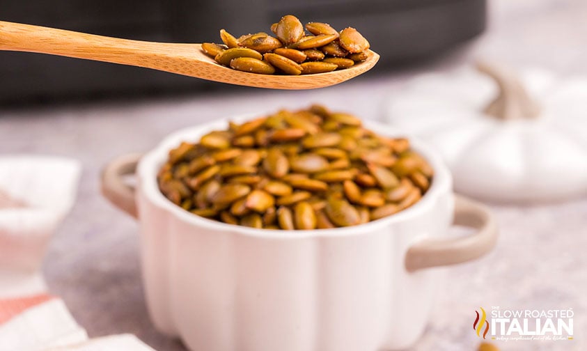 spoonful of air fried pumpkin seeds with pumpkin-shaped dish full in the background