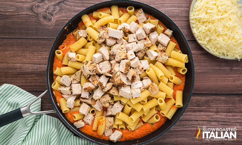 adding cubed chicken and cooked pasta to sauce in a skillet