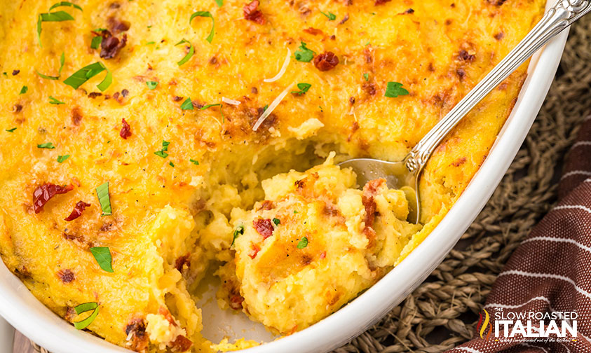 closeup of a serving spoon of baked mashed potatoes in a casserole dish