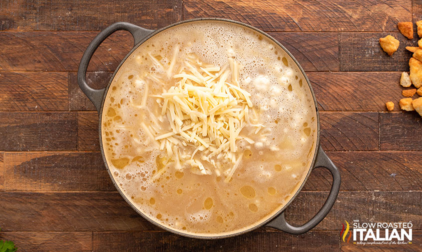 adding shredded cheese to chicken cordon bleu soup in a large pot