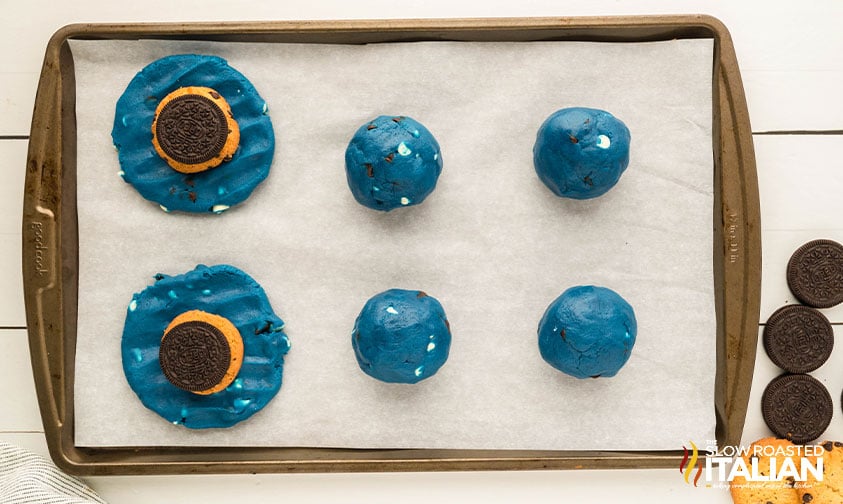 balls of cookie monster cookie dough on a parchment lined baking sheet with oreo and chocolate chip cookie inside