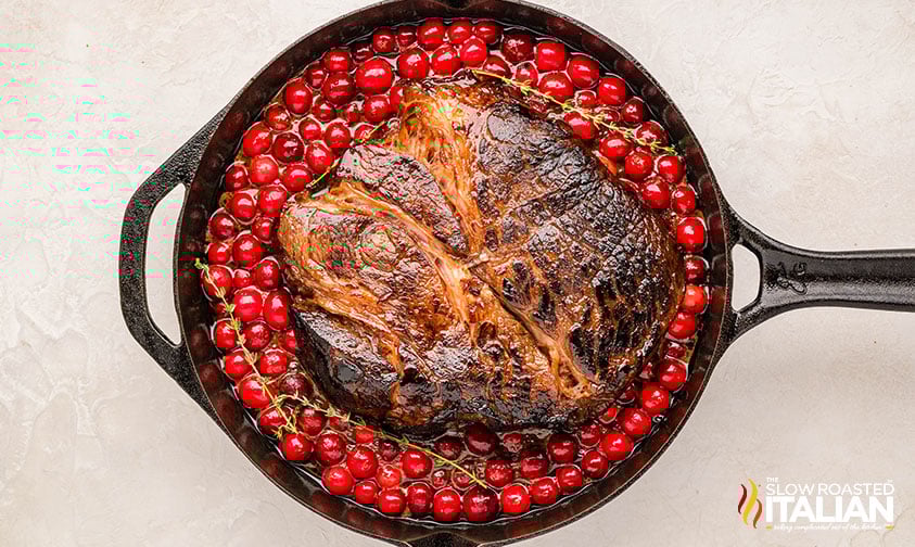 seared christmas roast added to cranberry sauce in cast iron skillet
