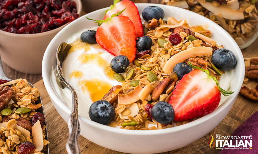 homemade granola added to a bowl of yogurt with fresh berries