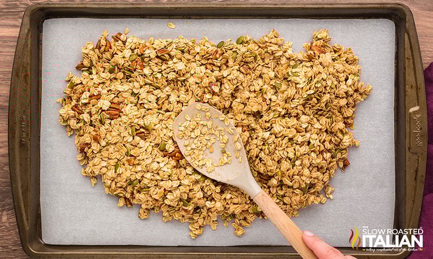 spreading homemade granola out on a parchment lined baking sheet