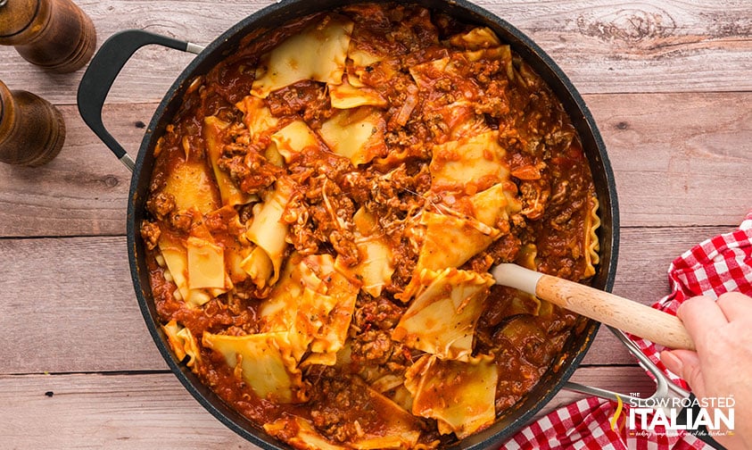 adding cooked pasta to meat sauce in a large pot