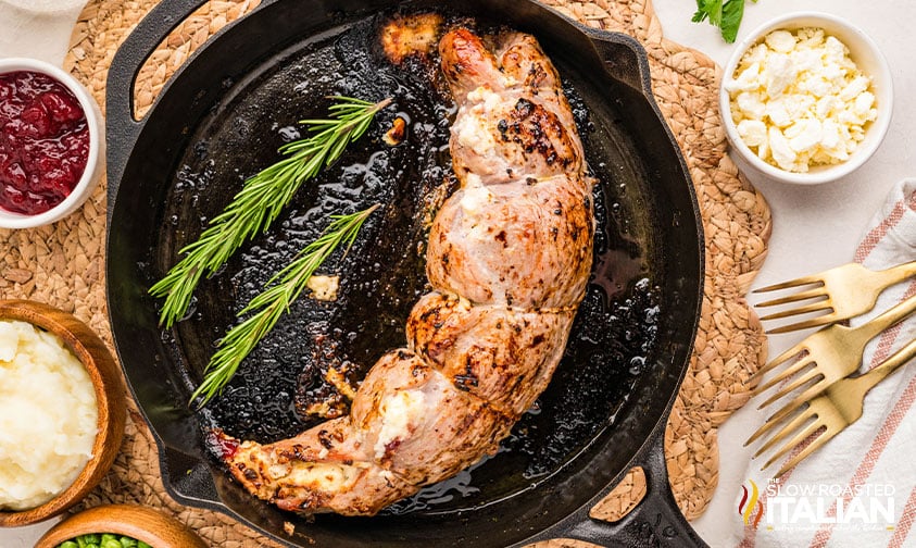 cooked stuffed pork tenderloin in a skillet with sprigs of rosemary