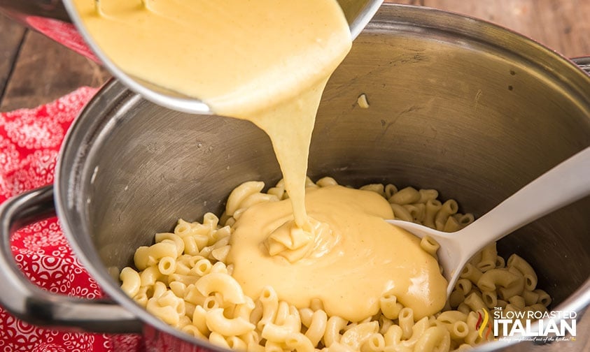 pouring cheese sauce from saucepan into a pot of cooked macaroni