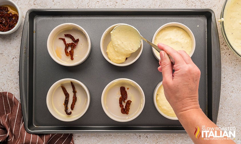 adding sun dried tomatoes and ricotta mixture to ramekins on a baking sheet