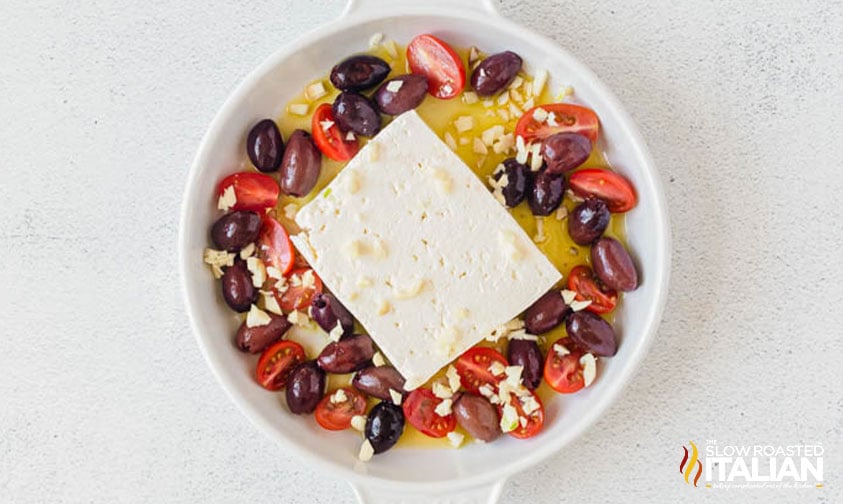 block of feta cheese, olives, tomatoes and oil for baked feta in a round baking dish