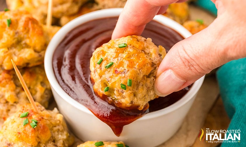 hand dipping a sausage popper into a small bowl of sauce
