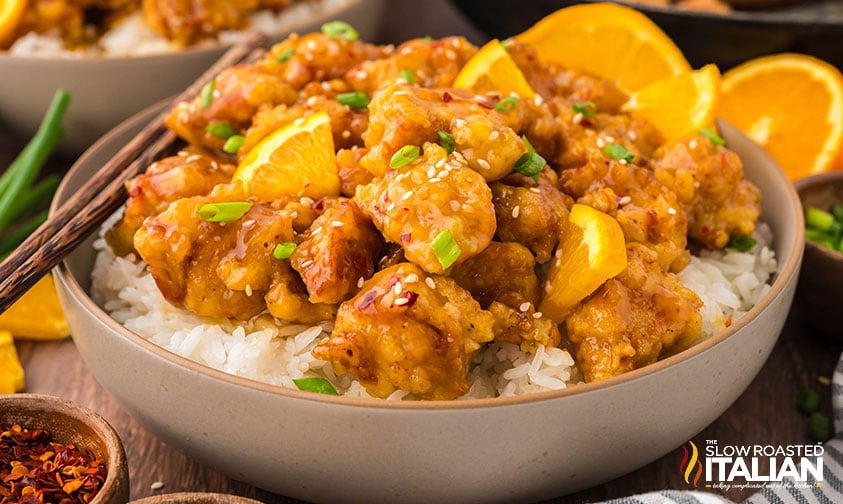 bowl of simple orange chicken over a bed of rice in a bowl garnished with orange slices
