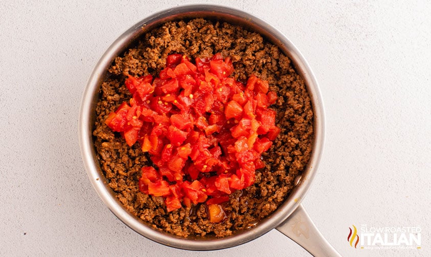 adding a can of rotel to cooked ground beef in a skillet