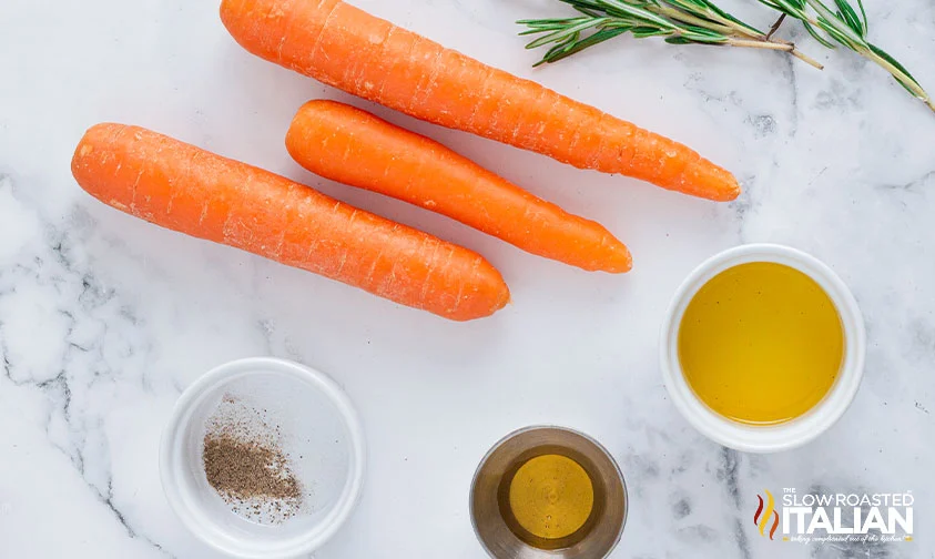 whole carrots and rosemary sprig next to bowls of oil, honey, and seasonings