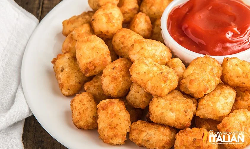 air fryer frozen tater tots piled onto a plate with bowl of ketchup in the middle