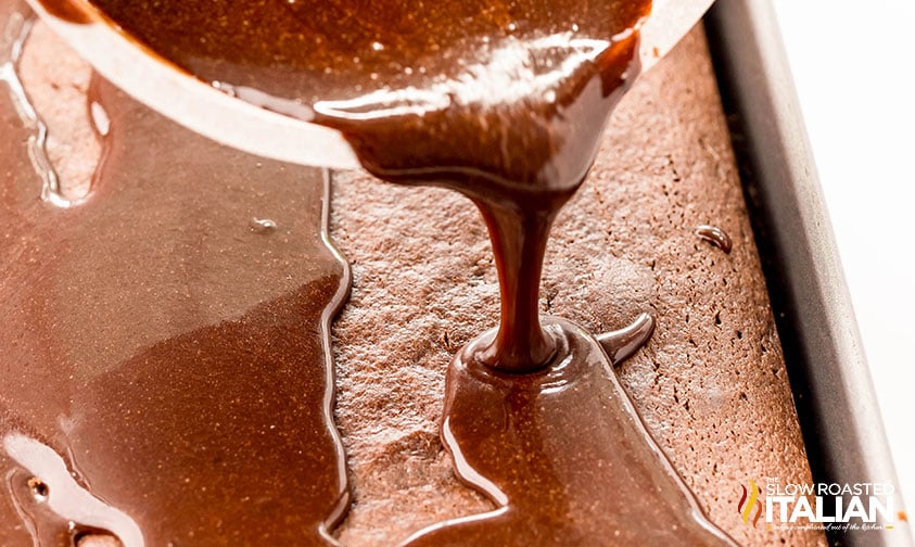 pouring warm frosting evenly over chocolate dr pepper cake