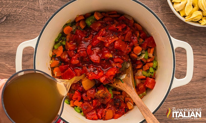 adding vegetable stock and diced tomatoes to large pot of vegetable tortellini soup