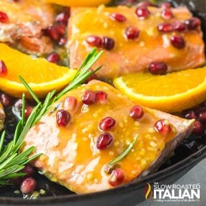 closeup of orange glazed salmon with rosemary, pomegranate seeds and sliced oranges in a skillet