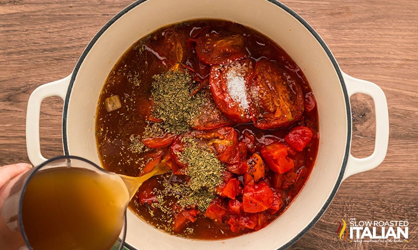 adding roasted tomatoes, seasonings and chicken stock to large pot of roasted tomato soup