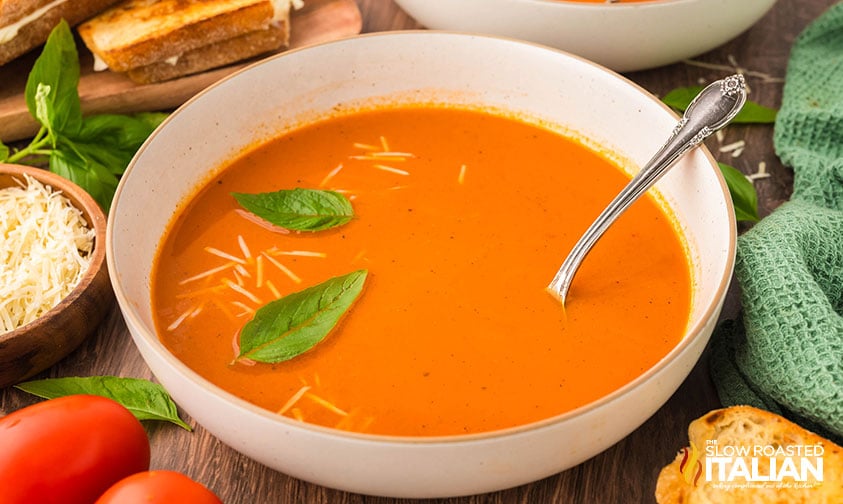 large bowl of roasted tomato soup with basil leaves and shredded cheese