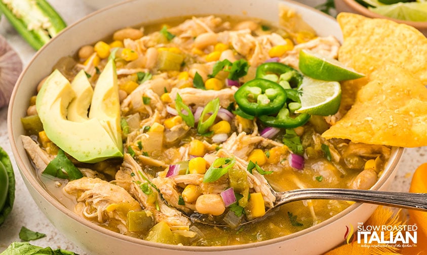 large bowl of salsa verde chicken soup topped with avocado, jalapenos and corn chips