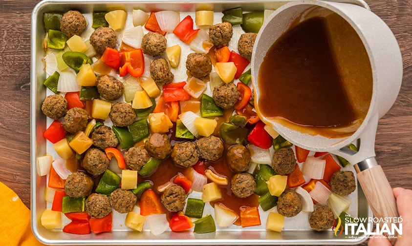 drizzling sweet and sour sauce over meatballs and veggies on a sheet pan