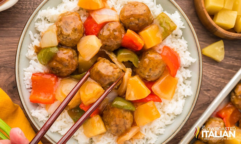 closeup of sweet and sour meatballs with pineapple chunks, peppers and onions over a bed of rice