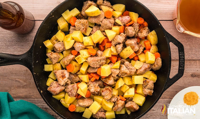 vegetables added to pork stew in a cast iron skillet