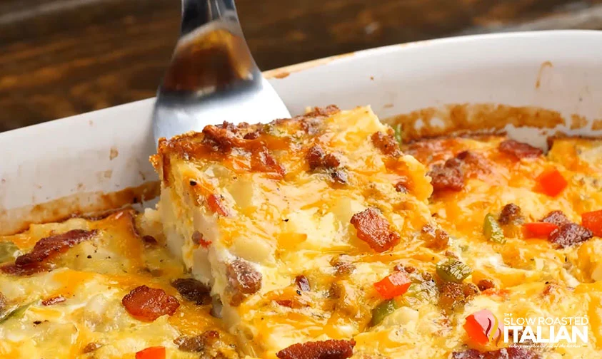 lifting a slice of bacon and egg casserole from baking dish