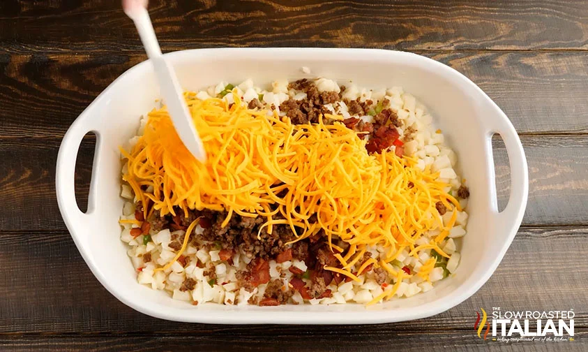 layering shredded cheese, bacon, sausage, and potatoes in baking dish for breakfast casserole