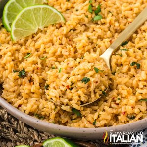 closeup of a bowl of spicy rice with a spoon and lime slices
