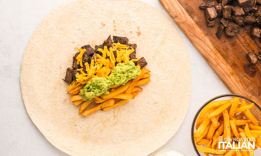 adding guacamole and shredded cheese to a calafornia burrito