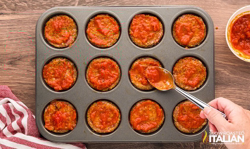 adding pasta sauce to meatloaf cups with a spoon