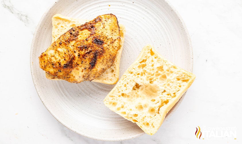 seasoned chicken cutlet on half of a ciabatta roll making a chicken caprese sandwich