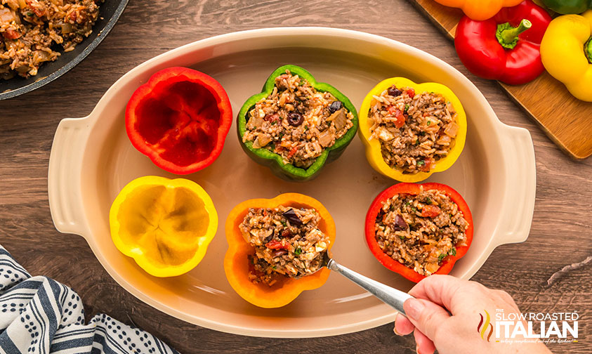 filling greek stuffed peppers in a baking dish