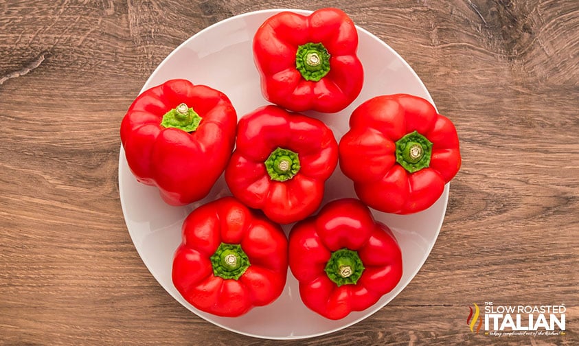 five red peppers sitting on a white plate to used for roasted red peppers