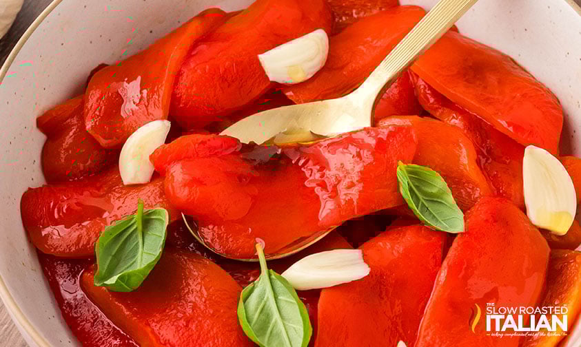 seasoned roasted red peppers in a bowl with basil and cloves of garlic