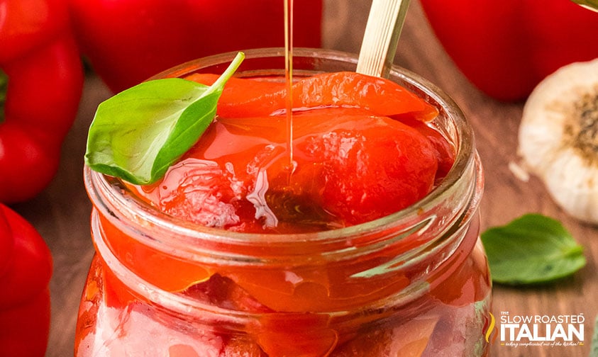 drizzling oil over roasted red peppers in a glass jar