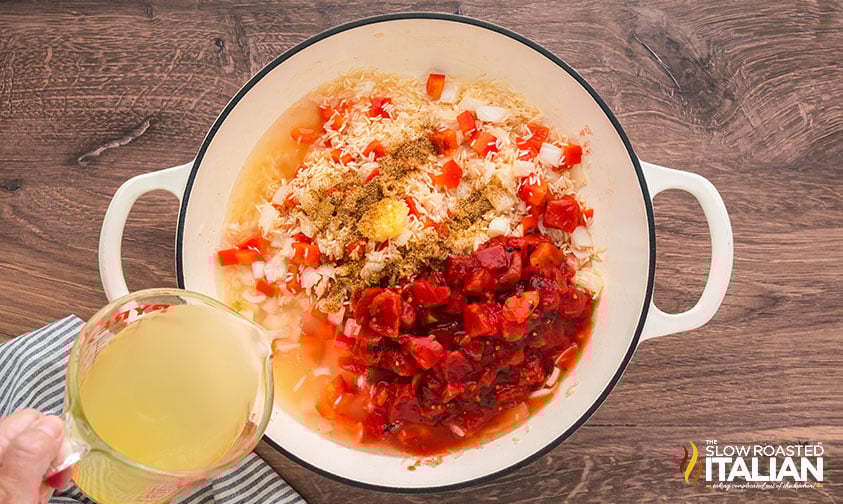 adding chicken stock to cajun shrimp and rice in a large pot