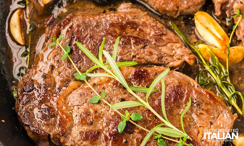 closeup of boneless steak recipe with a sprig of rosemary and garlic cloves