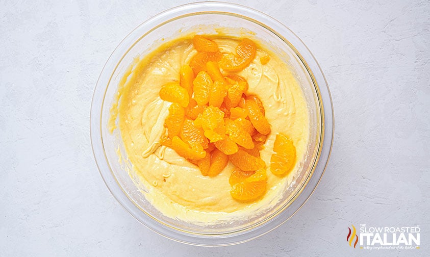 adding oranges to pig pickin cake batter in a glass bowl