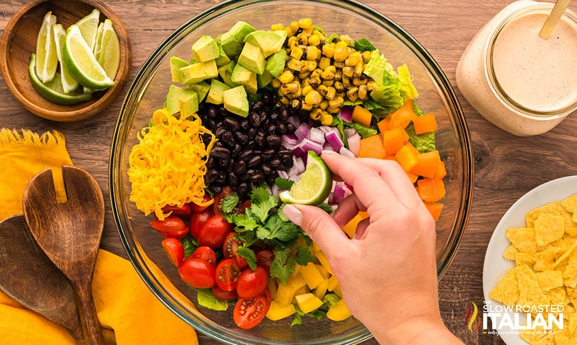 ingredients for southwest chopped salad in a large bowl with dressing and sliced limes on the side